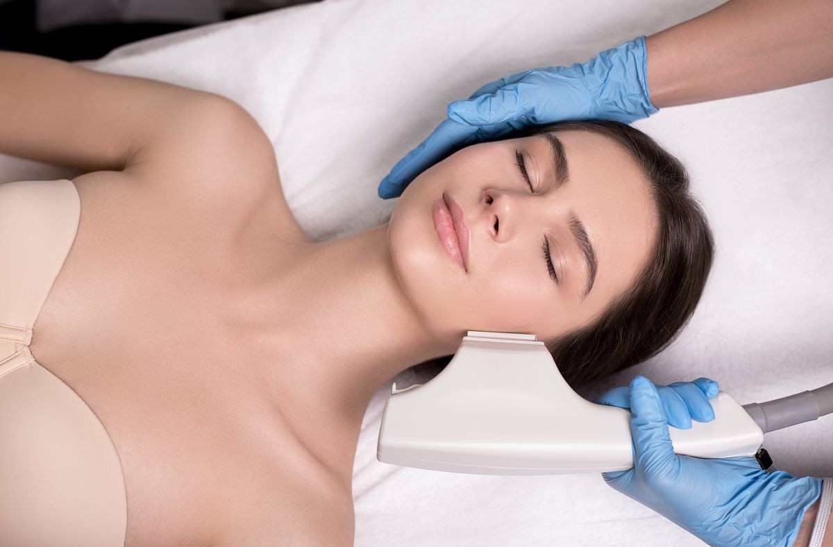 Skin care concept. Hardware cosmetology. Close up picture of attractive woman with fresh freckled skin receiving rf lifting procedure in a beauty centre.